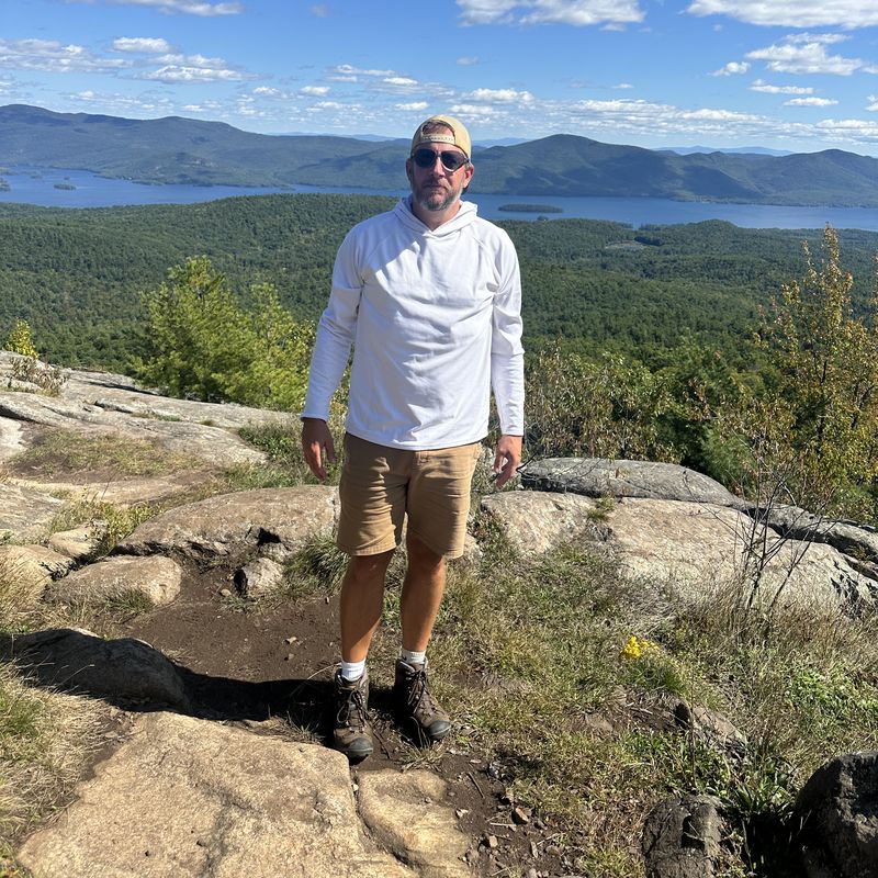 Jared on a rocky overlook above a lake and mountains