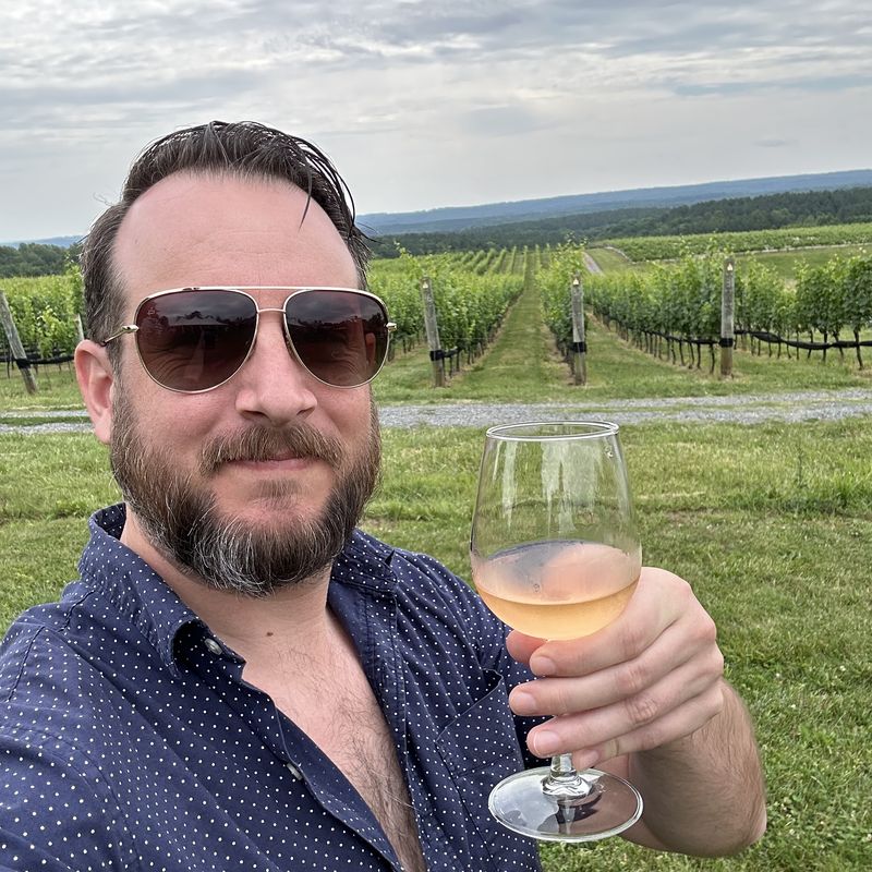 Jared raising a glass of wine in front of vineyard rows